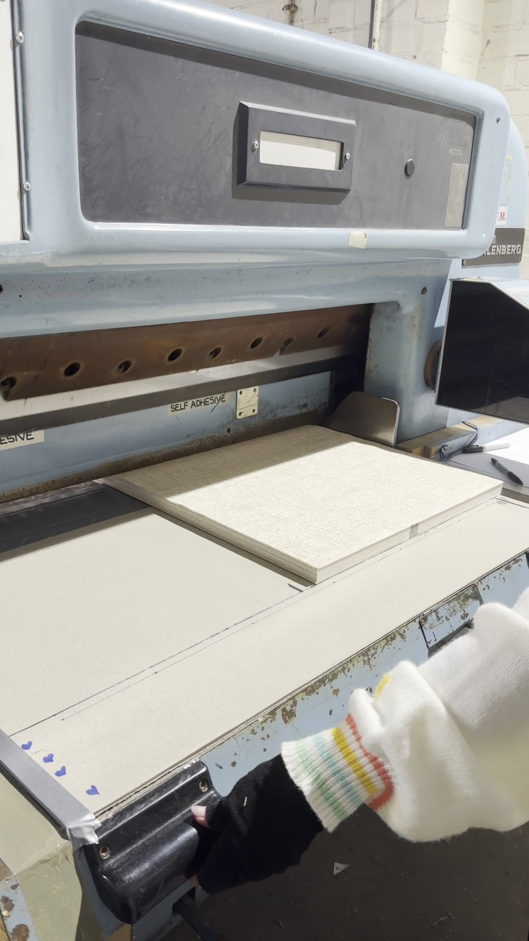 Maker squaring a stack of fabric-faced board on the guillotine bed before cutting