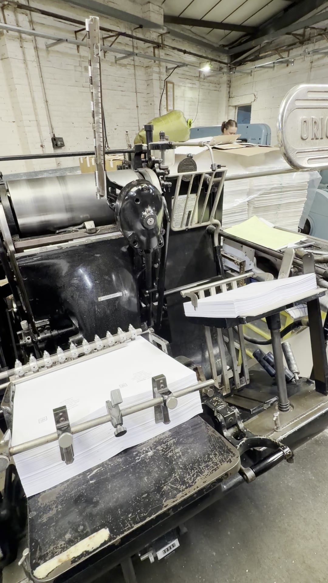 A working Heidelberg cylinder press surrounded by stacks of sheets in the Swatch Studio factory