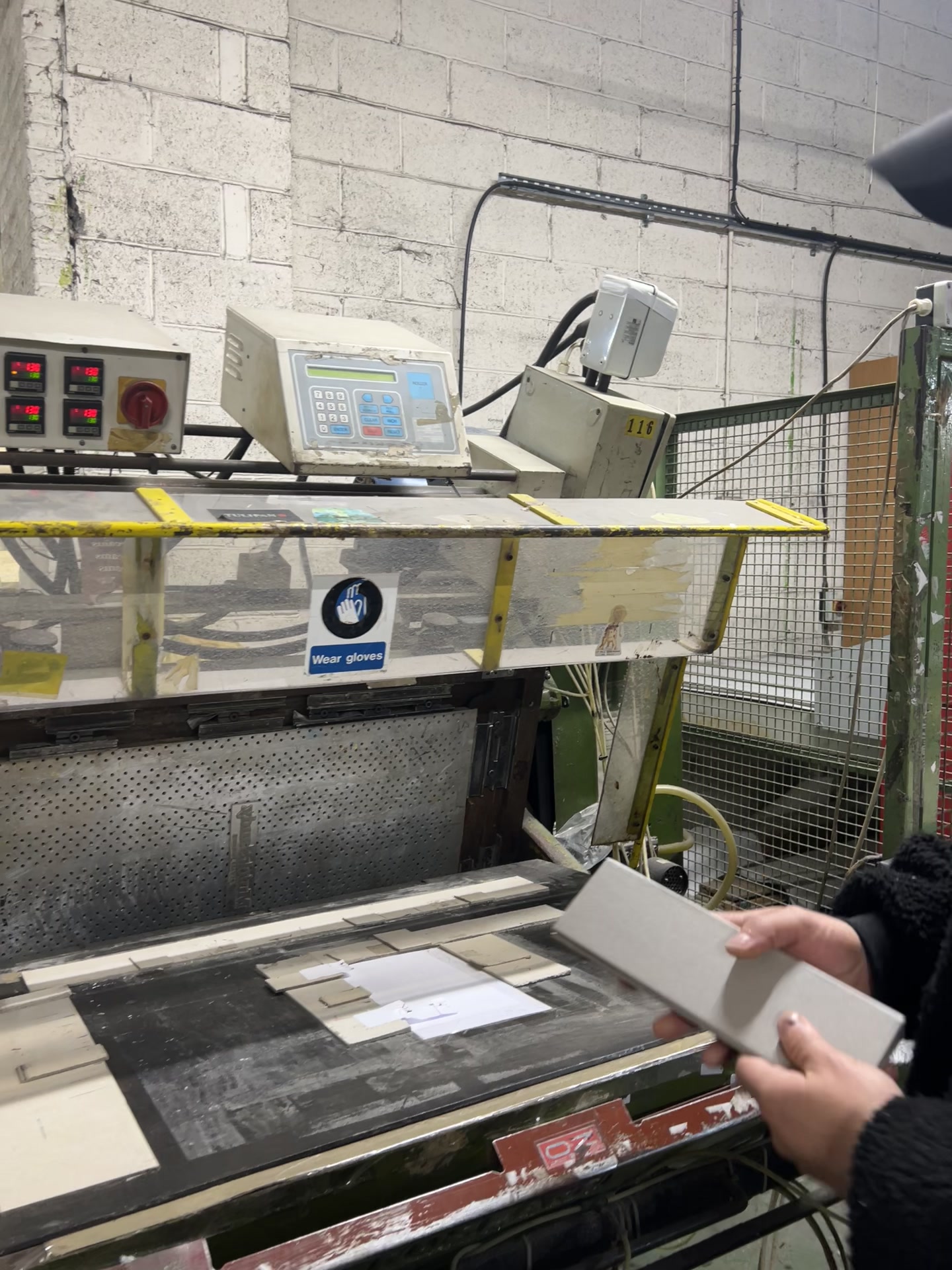 Maker holding a grey sample-book component beside the workshop heat-seal press